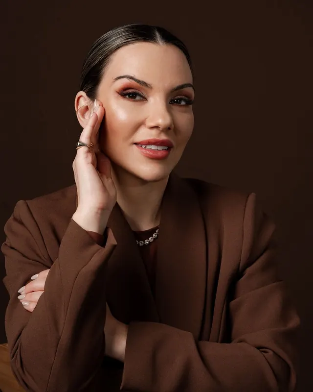 Dra. Marina Dresch sentada, de blazer marrom, com a mão no rosto